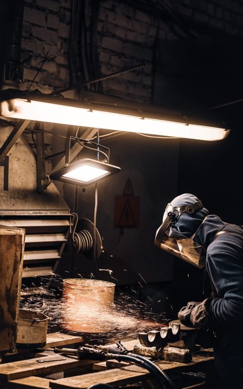 Man in protective mask is cutting metal and sparks are flying away.